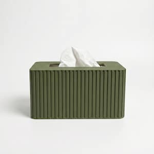 May include: A rectangular olive green tissue box cover featuring a vertical ribbed texture on all visible sides. The top surface has a central rectangular opening from which a single white paper tissue is protruding upwards in a folded shape.