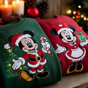 Może przedstawiać: Dwie świąteczne bluzy, jedna zielona i jedna czerwona, z Myszka Miki i Myszka Minnie w strojach Świętego Mikołaja. Zielona bluza ma Myszka Miki trzymającego laskę cukrową i choinkę. Czerwona bluza ma Myszka Minnie trzymającą prezent.