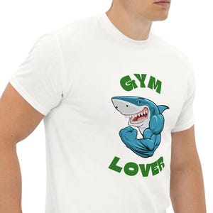 May include: White t-shirt with a green graphic of a blue shark with muscles flexing and the text "GYM LOVER"