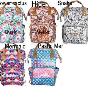 May include: Six different patterned diaper bags with personalized embroidery. The bags are all black with brown leather accents. The patterns include a floral cactus print, a cowhide print, a snake print, a mermaid print, a pastel mermaid print, and a unicorn print. The embroidery includes the words "Give Me", "Another", "Hank", "Unicorn", and "Cookie".