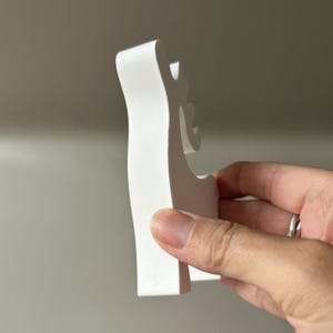 May include: A solid white, matte-finished wooden cutout in the shape of a stylized reindeer silhouette. The object features a smooth, flat surface with a distinct profile showing the head, antlers, and body, presented in a clean, minimalist aesthetic.