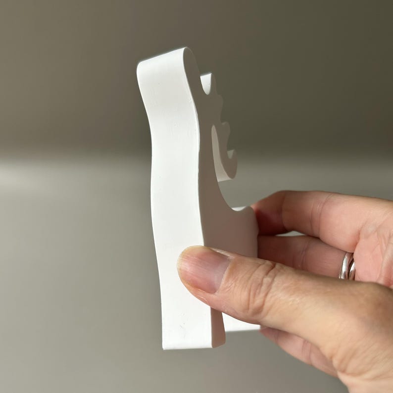 May include: A solid white, matte-finished wooden cutout in the shape of a stylized reindeer silhouette. The object features a smooth, flat surface with a distinct profile showing the head, antlers, and body, presented in a clean, minimalist aesthetic.