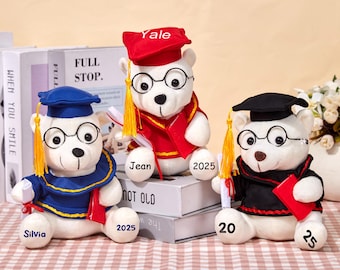 May include: Three white plush teddy bears wearing graduation caps and gowns. The bears are holding diplomas and have glasses on. The bears are named Yale, Jean, and Silvia. The year 2025 is written on the bears' gowns.