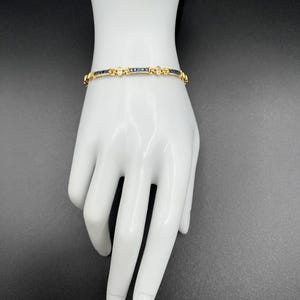 May include: A gold bracelet featuring a series of square-cut dark blue sapphires set in a channel style, interspersed with small, clear, round-cut accent stones. The metal links are polished gold, creating a continuous, flexible band design.