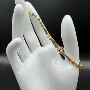 May include: A gold link bracelet featuring alternating segments of deep blue rectangular sapphires and small round clear diamonds. The bracelet is constructed with polished gold metal connectors and includes a secure box clasp mechanism.