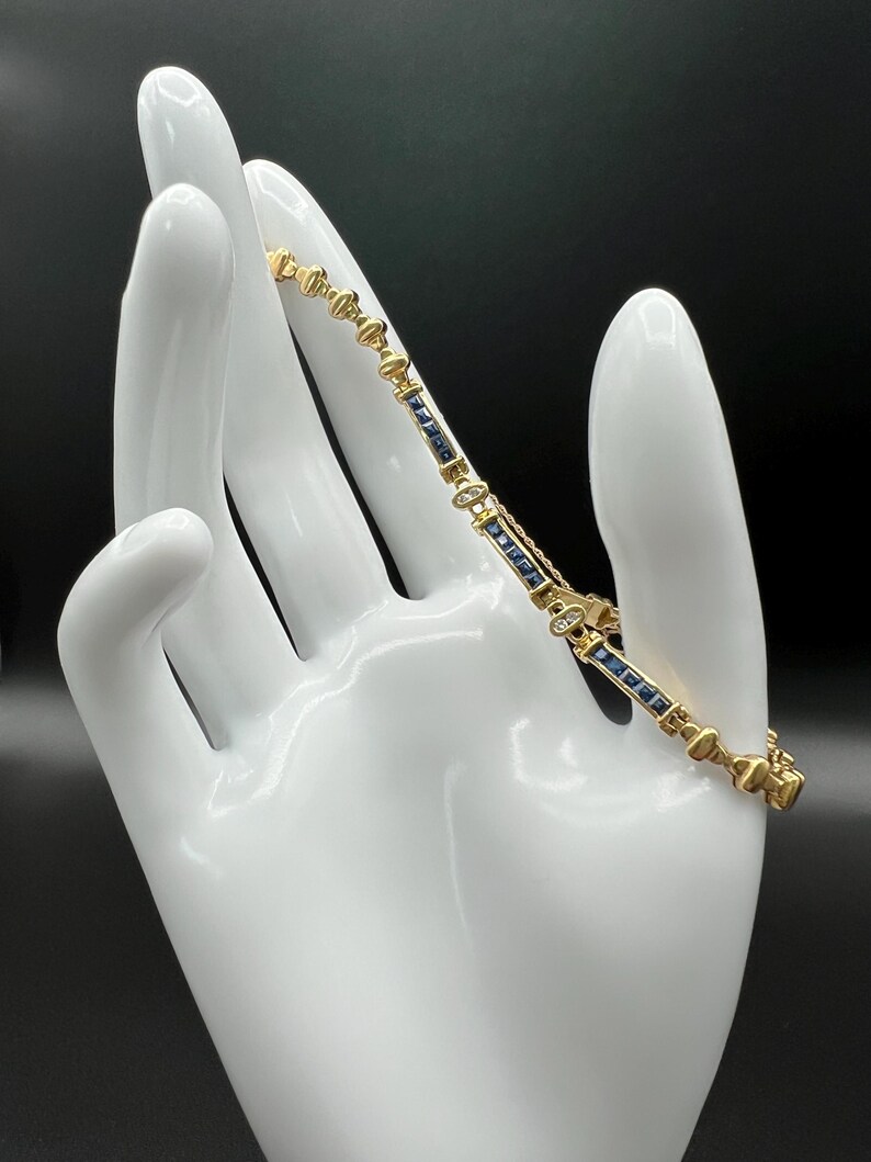 May include: A gold link bracelet featuring alternating segments of deep blue rectangular sapphires and small round clear diamonds. The bracelet is constructed with polished gold metal connectors and includes a secure box clasp mechanism.