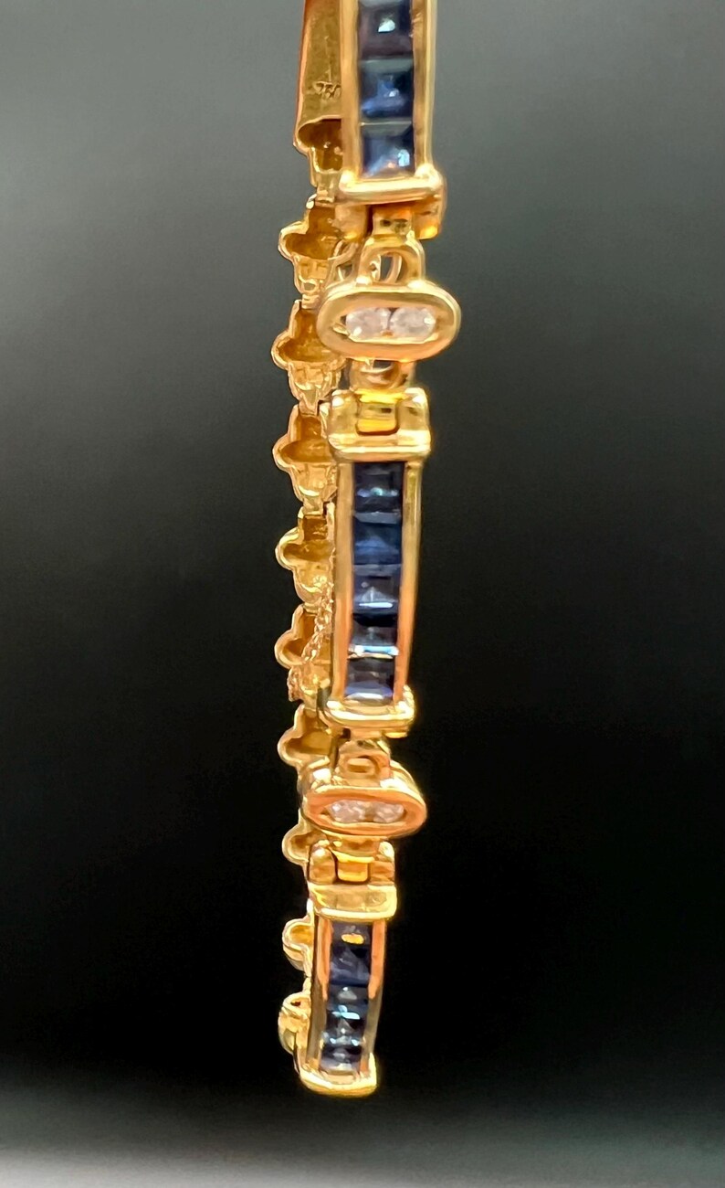 May include: A gold bracelet featuring a repeating pattern of rectangular channel-set blue sapphires alternating with oval links containing two small clear stones. The metal has a polished finish and the design includes decorative side elements.