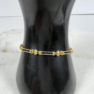 May include: A gold link bracelet featuring a repeating pattern of rectangular deep blue sapphire gemstones and small round clear diamonds set in gold metal. The bracelet consists of alternating blue stone segments and gold links with diamonds.