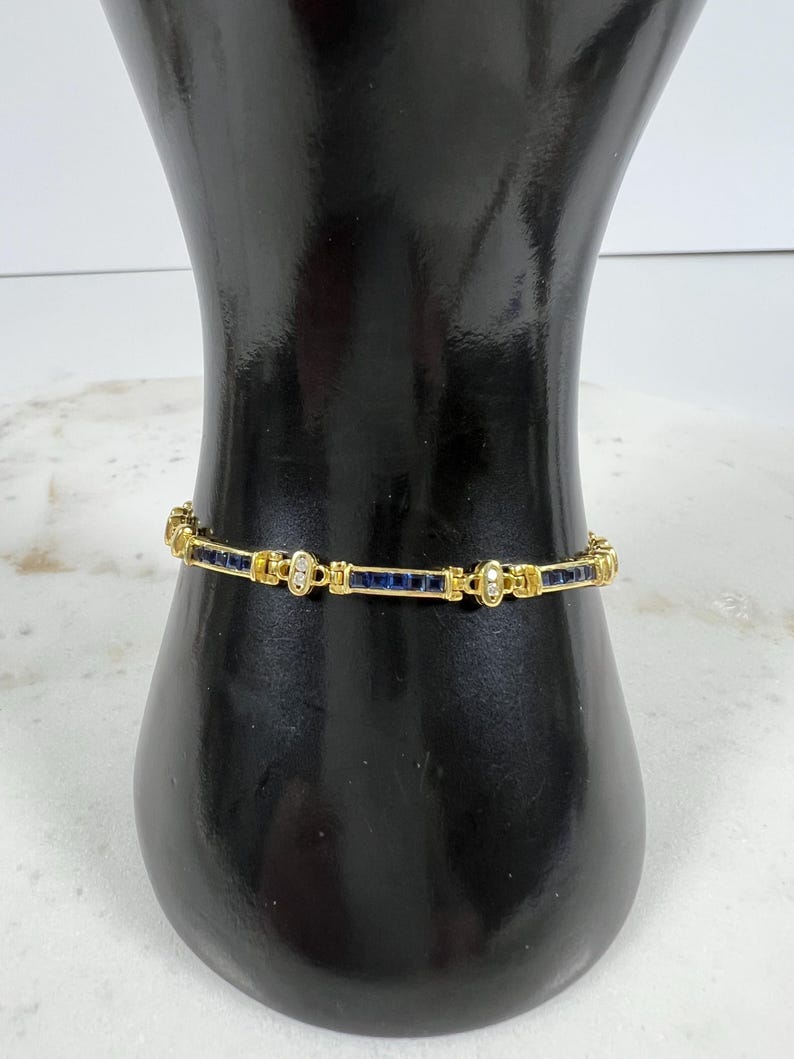 May include: A gold link bracelet featuring a repeating pattern of rectangular deep blue sapphire gemstones and small round clear diamonds set in gold metal. The bracelet consists of alternating blue stone segments and gold links with diamonds.