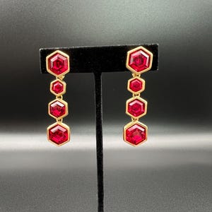 May include: A pair of gold earrings with dangling red hexagonal stones. Each earring has five stones.