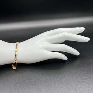 May include: A gold-toned bracelet featuring a repeating pattern of rectangular dark blue stones and small, circular gold-toned accents. The bracelet is constructed with a series of linked segments that alternate between the blue stones and gold metal.