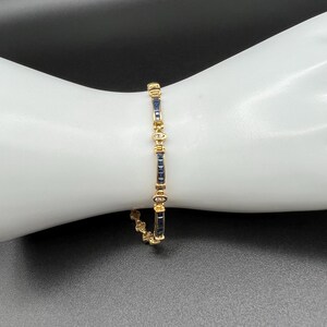 May include: A gold link bracelet featuring alternating rectangular dark blue sapphire gemstones and small clear round diamonds. The design consists of repeating segments of channel-set sapphires separated by circular metal links containing diamonds.