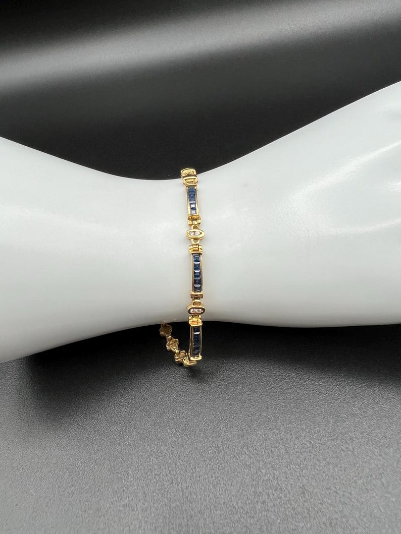 May include: A gold link bracelet featuring alternating rectangular dark blue sapphire gemstones and small clear round diamonds. The design consists of repeating segments of channel-set sapphires separated by circular metal links containing diamonds.