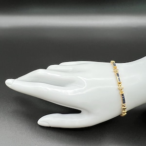 May include: A gold-toned link bracelet featuring alternating rectangular dark blue stones and small clear round stones. The bracelet is constructed with a series of metal segments that connect the blue and clear stones in a repeating pattern.