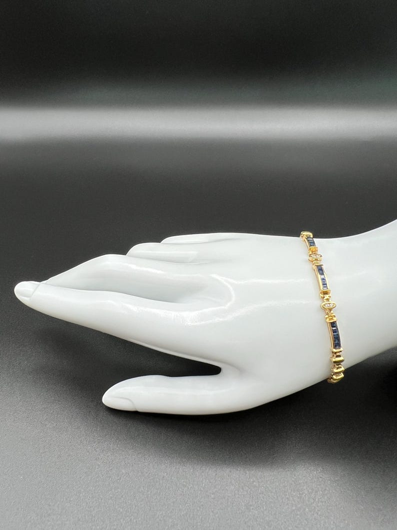 May include: A gold-toned link bracelet featuring alternating rectangular dark blue stones and small clear round stones. The bracelet is constructed with a series of metal segments that connect the blue and clear stones in a repeating pattern.