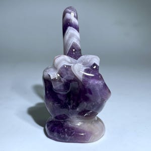 Könnte beinhalten: Ein violetter und weißer Amethystkristall, der in die Form eines Mittelfingers geschnitzt ist.