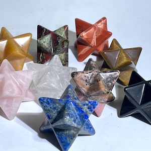 May include: A collection of ten star-shaped crystal points in various colors, including pink, white, brown, black, blue, and red. The crystals are arranged in a cluster on a white surface.