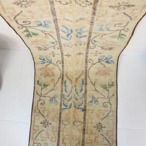 Pode incluir: Tapete corredor vintage creme com um padr&atilde;o floral em azul, verde e p&ecirc;ssego. O tapete tem formato retangular com borda marrom e provavelmente &eacute; feito de material tecido. O design apresenta flores e folhas estilizadas.