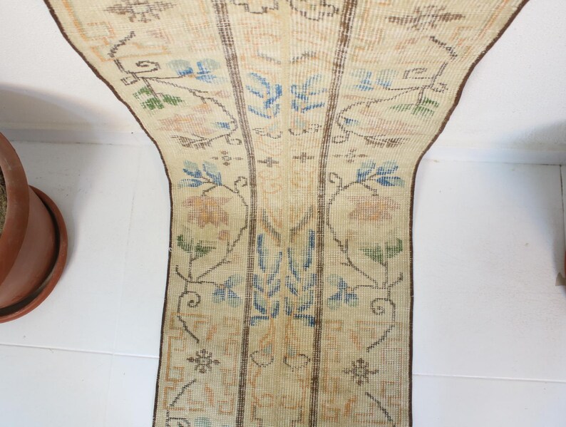 Pode incluir: Tapete corredor vintage creme com um padr&atilde;o floral em azul, verde e p&ecirc;ssego. O tapete tem formato retangular com borda marrom e provavelmente &eacute; feito de material tecido. O design apresenta flores e folhas estilizadas.