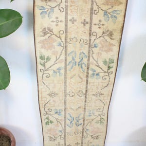 Pode incluir: Um tapete retangular vintage com fundo creme e intrincados padr&otilde;es florais em azul, verde e p&ecirc;ssego. O tapete apresenta um design central com listras verticais e uma borda marrom. O tapete &eacute; exibido verticalmente.