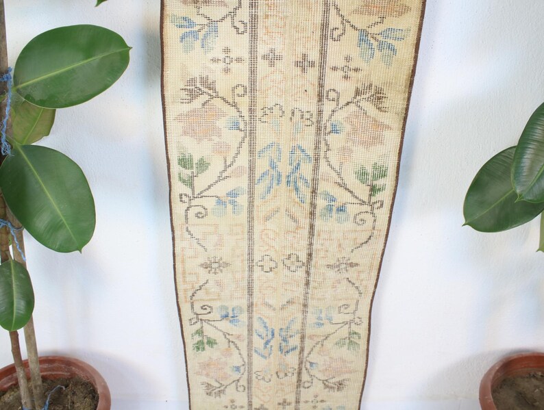 Pode incluir: Um tapete retangular vintage com fundo creme e intrincados padr&otilde;es florais em azul, verde e p&ecirc;ssego. O tapete apresenta um design central com listras verticais e uma borda marrom. O tapete &eacute; exibido verticalmente.