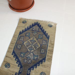 May include: A beige and blue patterned rug with a geometric design. The rug has a fringe border and is made of wool.