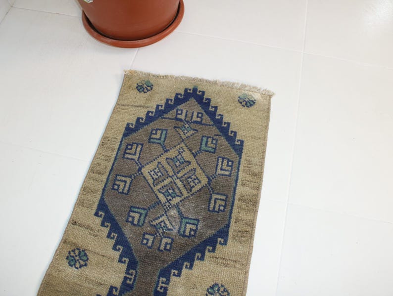 May include: A beige and blue patterned rug with a geometric design. The rug has a fringe border and is made of wool.