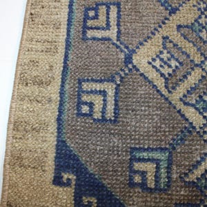 May include: Close-up of a rug with a geometric pattern in shades of blue, brown, and beige. The rug has a fringe border.
