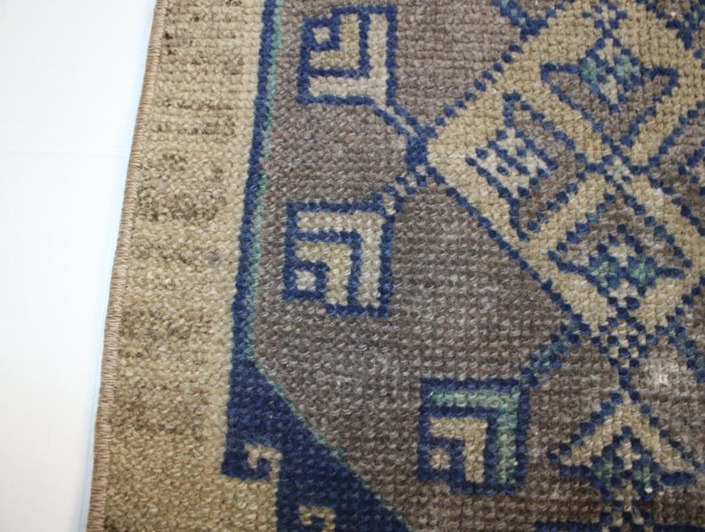 May include: Close-up of a rug with a geometric pattern in shades of blue, brown, and beige. The rug has a fringe border.