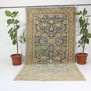 May include: A vintage rug with a blue and beige floral pattern. The rug has a faded look and is hanging on a wall.