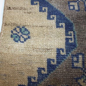May include: Close-up of a beige rug with a blue and gray geometric pattern. The rug has a fringe border.