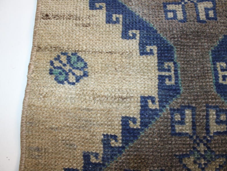 May include: Close-up of a beige rug with a blue and gray geometric pattern. The rug has a fringe border.