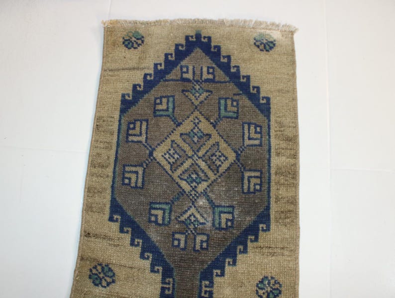 May include: A beige rug with a blue and brown geometric pattern. The rug has a fringed edge.