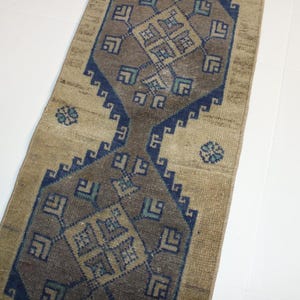 May include: A beige runner rug with a blue and brown geometric pattern. The rug has a traditional design with repeating motifs.