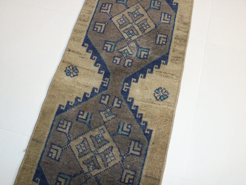 May include: A beige runner rug with a blue and brown geometric pattern. The rug has a traditional design with repeating motifs.