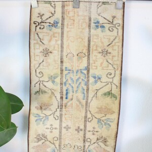 Pode incluir: Um tapete retangular vintage com fundo creme e intrincados padr&otilde;es florais em azul, castanho e p&ecirc;ssego. O tapete &eacute; orientado verticalmente e apresenta um design central com motivos florais sim&eacute;tricos e bordas.