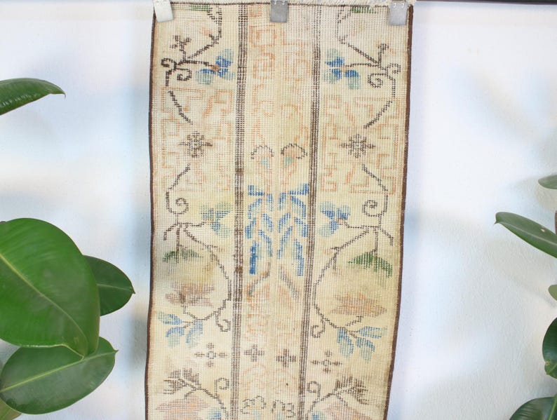 Pode incluir: Um tapete retangular vintage com fundo creme e intrincados padr&otilde;es florais em azul, castanho e p&ecirc;ssego. O tapete &eacute; orientado verticalmente e apresenta um design central com motivos florais sim&eacute;tricos e bordas.