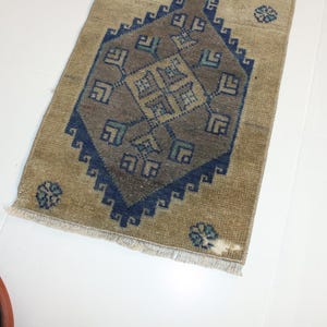 May include: A beige rug with a blue and brown geometric pattern. The rug has a fringe border.