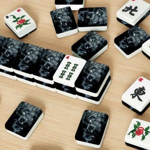 May include: A collection of Mahjong tiles with black and white designs. Some tiles feature a smoky pattern, while others display Chinese characters or floral illustrations. The tiles are arranged on a light wooden surface.