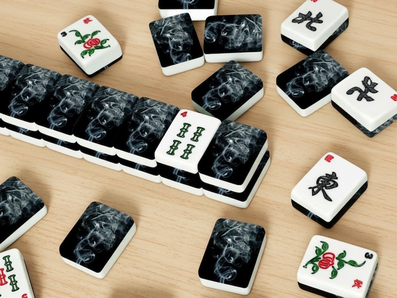 May include: A collection of Mahjong tiles with black and white designs. Some tiles feature a smoky pattern, while others display Chinese characters or floral illustrations. The tiles are arranged on a light wooden surface.