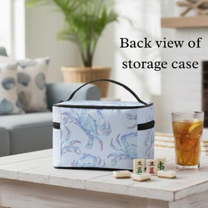 May include: A light blue storage case with a black handle and zipper, featuring a pattern of blue crabs. The text "Back view of storage case" is visible. The case sits on a white table with a glass of iced tea and Mahjong tiles.