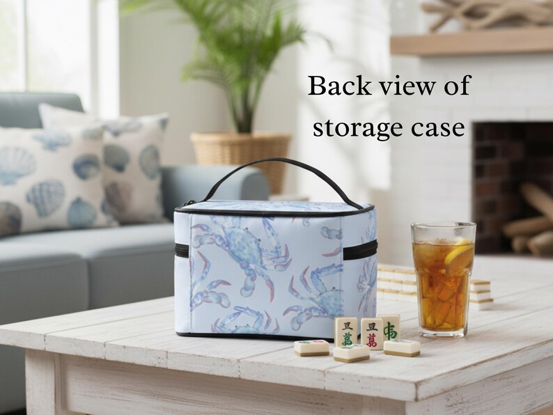 May include: A light blue storage case with a black handle and zipper, featuring a pattern of blue crabs. The text "Back view of storage case" is visible. The case sits on a white table with a glass of iced tea and Mahjong tiles.