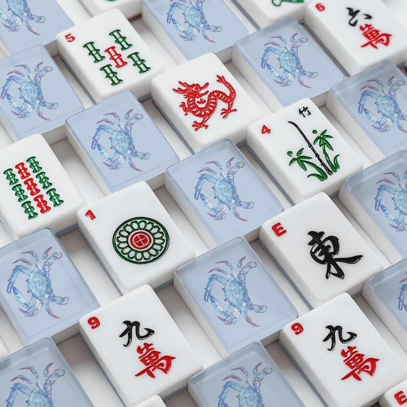 Puede incluir: Una colecci&oacute;n de fichas de Mahjong blancas con varios s&iacute;mbolos y caracteres. Algunas fichas presentan dragones rojos, bamb&uacute; verde e ilustraciones de cangrejos azules. Las fichas est&aacute;n dispuestas en un patr&oacute;n de cuadr&iacute;cula, mostrando los componentes del juego.