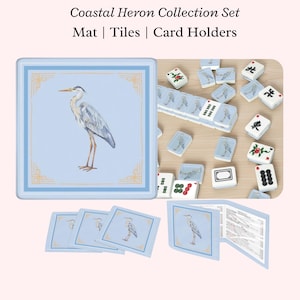May include: Coastal Heron Collection Set. A light blue mat and card holders with a heron illustration. The set includes tiles with heron and floral designs. The text on the image reads: Coastal Heron Collection Set Mat | Tiles | Card Holders.