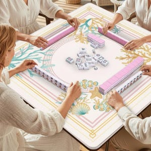 May include: A square Mahjong table with a cream-colored surface featuring a coral reef design in teal, gold, and pink. Four people are playing Mahjong, with pink tile racks and white tiles visible. The game is set on a wooden table.