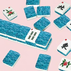 May include: A collection of Mahjong tiles with a blue water-like design and white tiles with red and black symbols and floral patterns. The tiles are scattered on a light pink background.