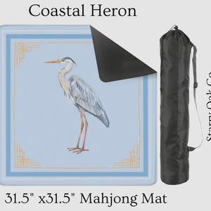 May include: A 31.5" x 31.5" Mahjong mat featuring a watercolor illustration of a Coastal Heron. The mat has a light blue background with a decorative border and a black carrying case. The text "Coastal Heron" is at the top.