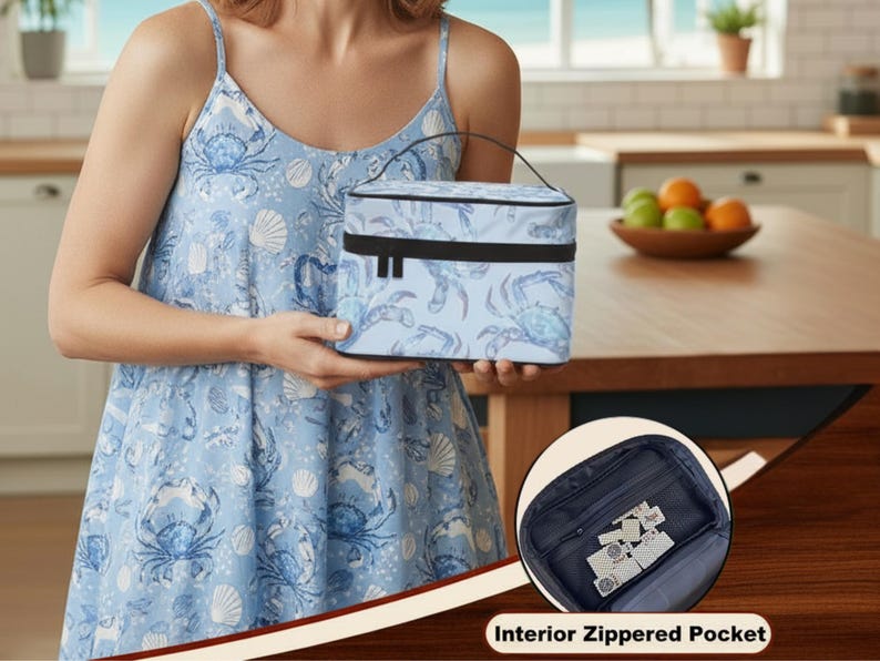May include: A light blue insulated lunch bag with a crab and seashell pattern. The bag has a black handle and trim. The image also shows a close-up of the interior zippered pocket. The bag is held by a person wearing a blue dress with a matching crab and seashell pattern.
