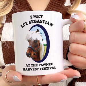 May include: White ceramic mug with a brown and white horse illustration and the text "I met Lil' Sebastian at the Pawnee Harvest Festival".