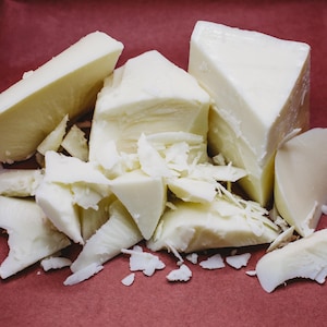 May include: A close-up of white cheese broken into pieces on a red surface. The cheese is in various shapes and sizes, some are large chunks and others are small, thin pieces.